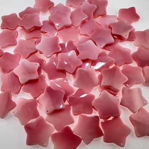 May include: A collection of numerous small, five-pointed star-shaped beads in various shades of pink. Each individual bead features a smooth, glossy finish and a single small hole near one of the points, suitable for threading or crafting projects.