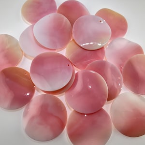 Könnte beinhalten: Eine Sammlung runder, flacher Muschelkomponenten in verschiedenen Schattierungen von zartem Rosa und Weiß. Jedes Stück hat eine glatte, schimmernde Oberfläche mit einem kleinen Loch nahe dem Rand, geeignet für Schmuckherstellung und Bastelprojekte.