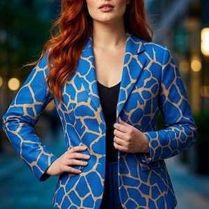 Op de afbeelding: Een felblauwe blazer met een beige girafachtig patroon, gestructureerde revers en lange mouwen. Het jasje wordt gedragen over een eenvoudig zwart topje en gecombineerd met een donkerblauwe broek, wat zorgt voor een samenhangend geheel met een opvallende print.