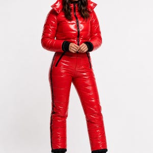 May include: A shiny red snowsuit with a hooded jacket and matching pants. The jacket has a black zipper and cuffs, and the pants have black stripes down the sides. Black boots complete the winter outfit.