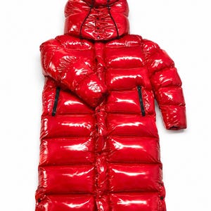 May include: A long, glossy red puffer coat with a hood and black zippers. The interior of the hood is a bright blue. The coat is designed to be floor-length and has a shiny, reflective surface.