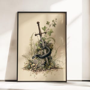 Op de afbeelding: Een ingelijste kunstdruk met een gedetailleerde illustratie van een metalen zwaard dat in een bemoste steen steekt. Een donkere, getextureerde slang is om het lemmet en de steen gewikkeld, omringd door groene varens, klimopbladeren en kleine paddenstoelen.