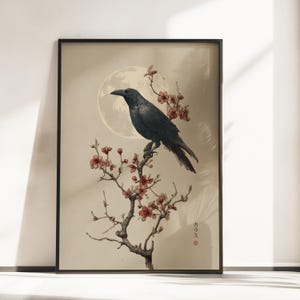 Könnte beinhalten: Ein gerahmter Kunstdruck, der eine schwarze Krähe auf einem blühenden Ast vor einem großen, blassen Mond zeigt. Der Hintergrund ist in einem neutralen Beigeton gehalten. Der japanische Text "カラス" steht unten rechts neben einem roten Punkt.