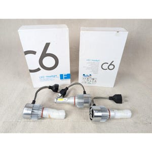 May include: Two white rectangular boxes labeled C6 LED Headlight and three silver metal LED headlight bulbs with integrated cooling fins, black braided cables, and two-prong electrical plugs. The bulbs feature a cylindrical design.
