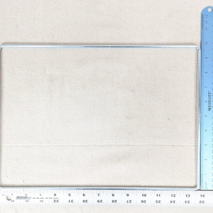 May include: A rectangular silver-colored metal frame positioned next to a blue Westcott ruler and a Johnson ruler. The metal frame measures approximately 12 inches in width and 9 inches in height based on the visible imperial measuring tools.
