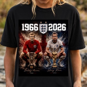 May include: A black t-shirt featuring a graphic print of two soccer players with trophies. The text reads 1966 Legends Then and 2026 Legends Now, with the names Bobby Moore and Harry Kane below. The England national team crest is centered at the top.