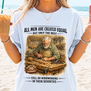 Könnte beinhalten: Hellblaues T-Shirt mit einer Grafik eines Holzwerkers und dem Text "ALL MEN ARE CREATED EQUAL BUT ONLY THE BEST". Die Grafik enthält den Text "LEVEL 70 WOODWORKER" und "STILL DO WOODWORKING IN THEIR SEVENTIES".