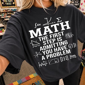 May include: A black t-shirt with white text and mathematical symbols. The text reads "MATH The First Step Is Admitting You Have A Problem". The shirt features various equations and diagrams.