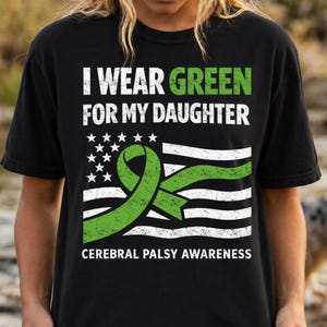 Peut inclure: T-shirt noir avec l'inscription "I WEAR GREEN FOR MY DAUGHTER" en blanc et vert. Le motif comprend un ruban vert et un drapeau américain, avec les mots "CEREBRAL PALSY AWARENESS" en bas.