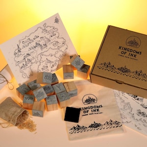 Peut inclure: Un kit d'artisanat sur le thème de la fantaisie avec une carte, des tampons et une boîte. Le kit comprend des tampons en bois avec des illustrations détaillées, une carte, un sac en toile et une boîte avec le texte "Kingdoms of Ink".