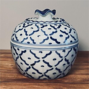 May include: A white ceramic jar with a lid, adorned with a blue floral pattern. The jar has a round shape with a lid that features a decorative handle. The blue and white color scheme gives it a classic, elegant look. The jar is likely used for storage or display.