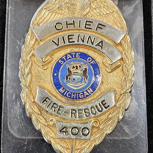 May include: A gold-toned metal badge featuring an eagle at the top, a central blue circular emblem with the State of Michigan seal, and silver banners reading CHIEF VIENNA and FIRE-RESCUE. The number 400 is at the bottom, with a nameplate reading STEVE DAVIDSON.