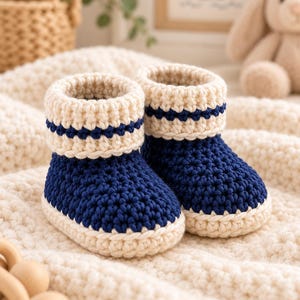 Puede incluir: Un par de patucos de ganchillo hechos a mano con la parte del pie en azul marino intenso y la suela de color crema. El puño del tobillo es de color crema con una distintiva raya horizontal azul marino en el centro de la textura tejida.