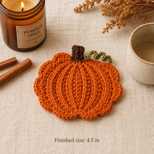 May include: A pumpkin-shaped crochet coaster in vibrant orange yarn with a dark brown stem and a small green curly vine. The coaster features a textured ribbed pattern and has a finished size of 4.5 inches as indicated by the text.
