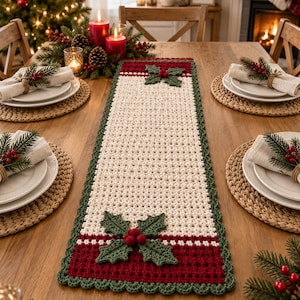 Pode incluir: Um caminho de mesa retangular de crochê com um centro na cor creme, bordas em vermelho escuro e um acabamento verde festonado. O caminho de mesa é decorado com duas aplicações de folhas de azevinho verdes e pequenas bagas vermelhas.
