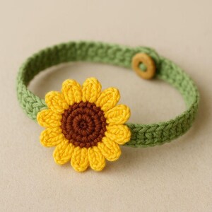 Könnte beinhalten: Ein handgefertigtes Häkelhalsband mit einer leuchtend gelben Sonnenblume und einem braunen Zentrum. Das Halsband ist grün und hat einen Holzknopfverschluss. Für Haustiere.