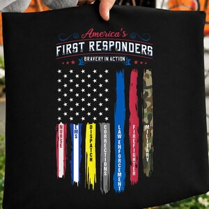 Może przedstawiać: Czarna koszulka z grafiką flagi amerykańskiej i pionowymi pasami reprezentującymi służby ratunkowe. Tekst głosi: America's FIRST RESPONDERS BRAVERY IN ACTION. Pasy są oznaczone: NURSE, EMS, DISPATCH, CORRECTIONS, LAW ENFORCEMENT, FIREFIGHTER, MILITARY.