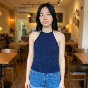 Könnte beinhalten: Eine Frau trägt ein marineblaues Neckholder-Top und Jeansshorts. Das Oberteil ist aus Strickstoff mit Rippstruktur. Der Hintergrund zeigt ein Café mit Holztischen und -stühlen.