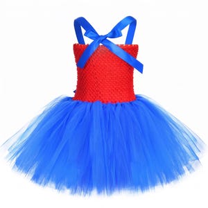 Op de afbeelding: Een mouwloze jurk met een felrood gehaakt lijfje en een volumineuze blauwe tule rok. Het lijfje is geaccentueerd met felblauwe satijnen lintbandjes die op de rug kruisen en in een strik worden vastgemaakt, wat een opvallend contrast cre&euml;ert.