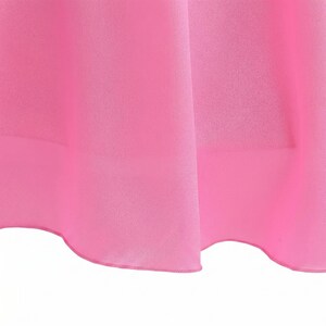 May include: Close-up of a vibrant pink fabric, possibly a dress or skirt, with soft folds and a delicate hemline. The material appears smooth and lightweight, with a subtle sheen. The bright color dominates the frame.