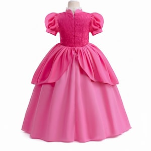 May include: A bright pink princess dress with a high collar and short, puffy sleeves. The bodice features a textured, lace-like design, and the skirt is layered with a full, flowing silhouette. The dress is designed for children.