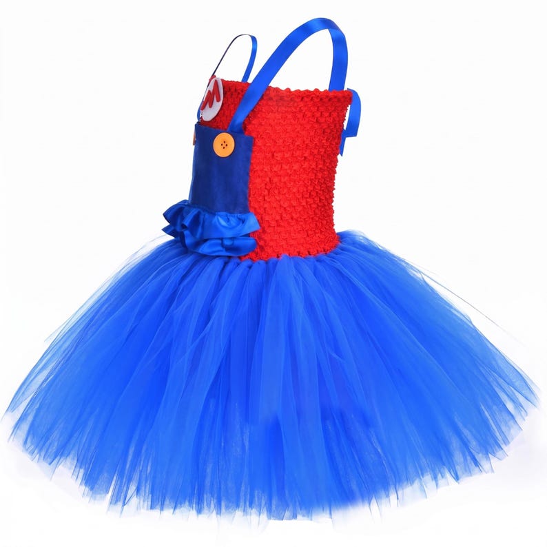 Op de afbeelding: Een jurk met een rood gehaakt lijfje, blauwe satijnen schouderbandjes en een blauw satijnen slabbetje aan de voorzijde. Het slabbetje heeft twee oranje knopen en een witte ronde patch met een rode letter M. De rok bestaat uit lagen blauwe tule.
