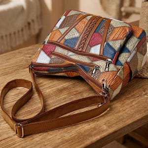 May include: A multi-colored crossbody bag featuring a patchwork design with triangular segments in shades of brown, blue, red, and white. The bag has a textured surface, multiple zippered compartments with silver-tone hardware, and a brown strap.