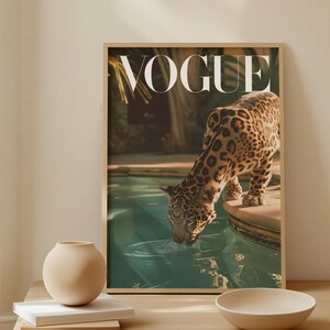 Könnte beinhalten: Ein gerahmtes Vogue-Magazin-Cover mit einem Jaguar, der Wasser trinkt. Das Bild hat eine warme Farbpalette und wird auf einem hellen Holztisch mit einer Vase, Büchern und einer Schüssel angezeigt.