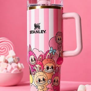 Pu&ograve; includere: Bicchiere Stanley a righe rosa e bianche con manico e coperchio rosa. Il bicchiere presenta un design a cartoni animati di conigli mostruosi e il logo Stanley. Un bicchiere a righe rosa e bianche con coperchio trasparente.
