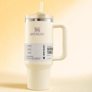 May include: Cream-colored Stanley Quencher tumbler with a handle and straw. The tumbler has the Stanley logo and text that reads "The Flawless Quencher Tumbler 40 oz / 1.1L". The tumbler is designed to keep drinks cold for 2 days and hot for 7 hours.