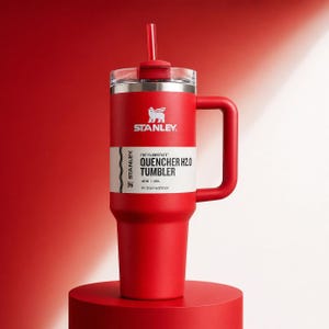 K&ouml;nnte beinhalten: Ein roter Stanley Flowstate Quencher H2.0 Becher mit Griff und Strohhalm. Der Becher hat einen silbernen Rand und ein wei&szlig;es Etikett mit dem Text "QUENCHER H2.0 TUMBLER" und dem Stanley-Logo. Er fasst 1,18 L.