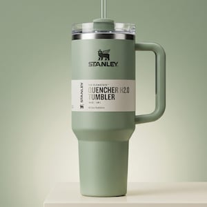 Op de afbeelding: Een saliegroene Stanley Quencher H2.0 Tumbler met een handvat en een rietje. De tumbler heeft een doorzichtig deksel en een wit label met de tekst "QUENCHER H2.0 TUMBLER" en het Stanley-logo. Hij bevat 1,18L.