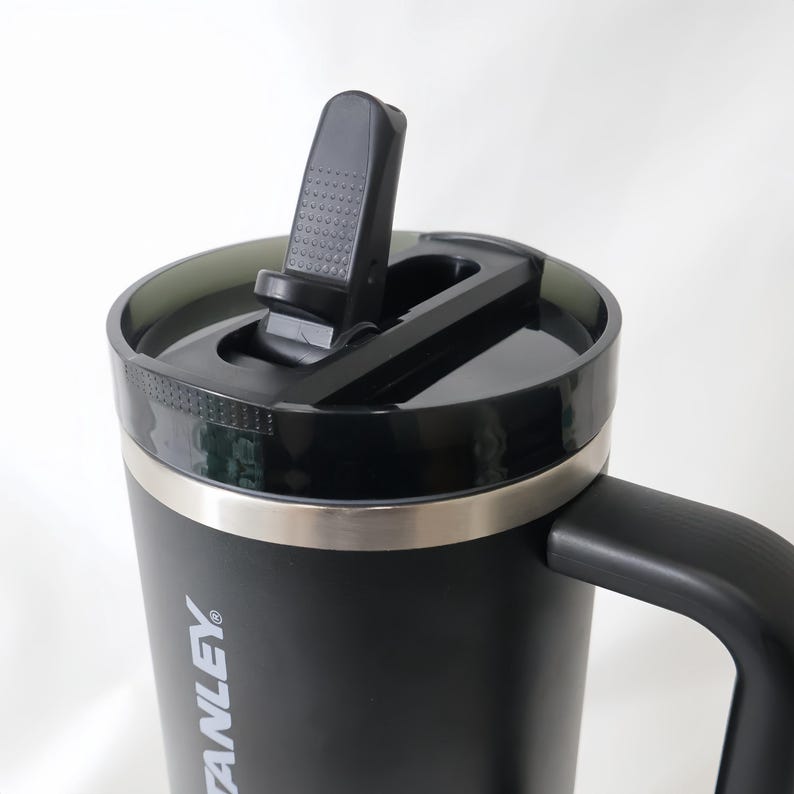 May include: Black insulated travel mug with a black handle and lid. The lid has a flip-top closure and a silver band around the top. The mug has the word "STANLEY" printed on the side.