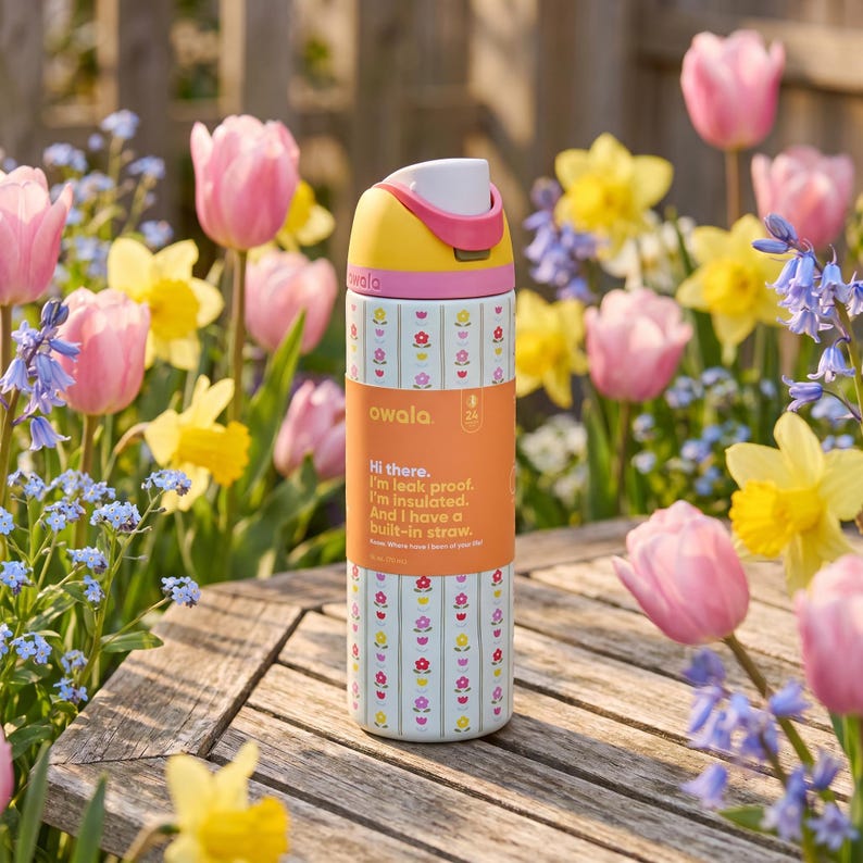Peut inclure: Une gourde Owala color&eacute;e avec un motif floral et un couvercle jaune, rose et blanc. La gourde a une paille int&eacute;gr&eacute;e et le texte "Hi there. I'm leak proof. I'm insulated. And I have a built-in straw."