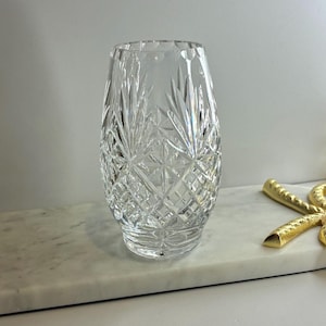 Könnte beinhalten: Eine klare, geschliffene Kristallvase mit einem Diamanten- und Blättermuster. Die Vase hat einen breiten Boden und verjüngt sich leicht nach oben. Die Vase steht auf einer weißen Marmoroberfläche.