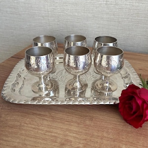 Puede incluir: Un juego de seis copas de metal plateado con patrones florales en relieve en los cuencos, dispuestas sobre una bandeja de servicio rectangular a juego con borde festoneado y diseño floral grabado en el centro.