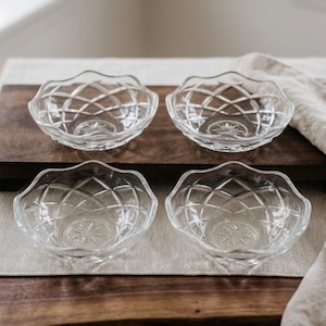 Pode incluir: Um conjunto de quatro taças de vidro transparente com borda recortada e um padrão de diamante prensado no exterior. Cada taça tem um design de estrela em relevo no centro da base interior, criando uma aparência reflexiva e texturizada.