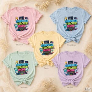 May include: Five short-sleeved crew neck t-shirts in pastel colors including pink, light blue, yellow, light green, and light purple. Each shirt features a graphic of a laptop with the text COMPUTER TEACHER MODE and Code-Create-Teach.