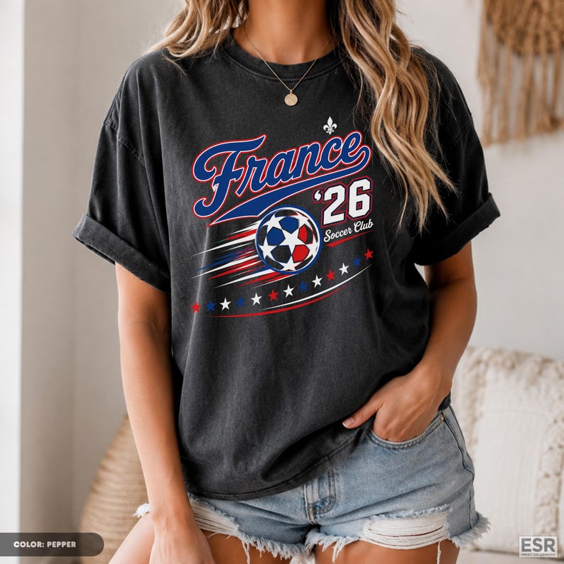 A woman wearing a black t-shirt with a graphic design featuring a soccer ball and stars, along with the text "France 26 Soccer Club".