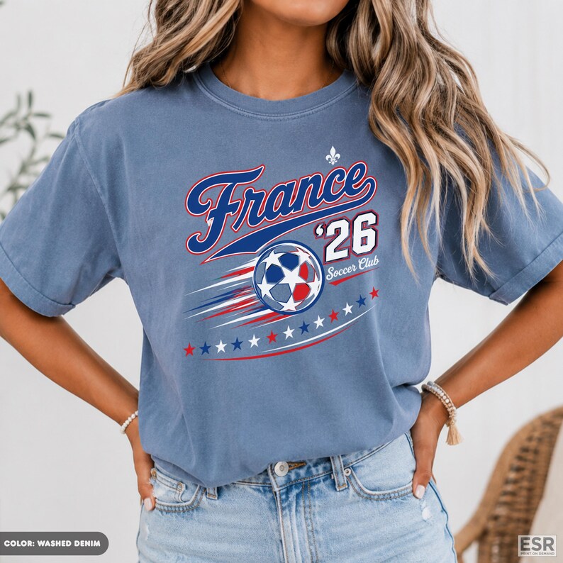 A woman wearing a blue t-shirt with a graphic design featuring a soccer ball and stars, along with the text "France '26 Soccer Club".