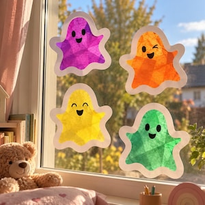 Könnte beinhalten: Vier durchscheinende, geisterförmige Fensteraufkleber in Violett, Orange, Gelb und Grün. Jeder Geist hat einen weißen Rand und ein einfaches schwarzes Gesicht mit zwei runden Augen und einem lächelnden Mund auf einer klaren Fensterscheibe.