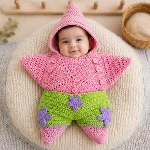 May include: A pink and lime green crocheted baby outfit shaped like a starfish. The top features a pointed hood and buttons, while the bottom section is lime green with three purple star-shaped appliqués. The garment has a textured knit finish.