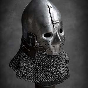 May include: A polished steel helmet featuring a rounded crown, a hinged face plate with two eye openings, and a perforated nose and mouth area. A dark leather strap secures the metal structure to a dense, silver-toned chainmail aventail.