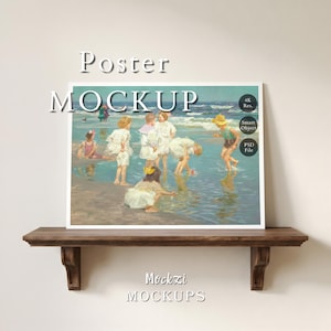 May include: A framed poster mockup featuring a painting of children playing at the beach. The artwork depicts figures in white clothing and hats, with the ocean in the background. The words "Poster Mockup" are above the artwork, and "Mockzi Mockups" are below.
