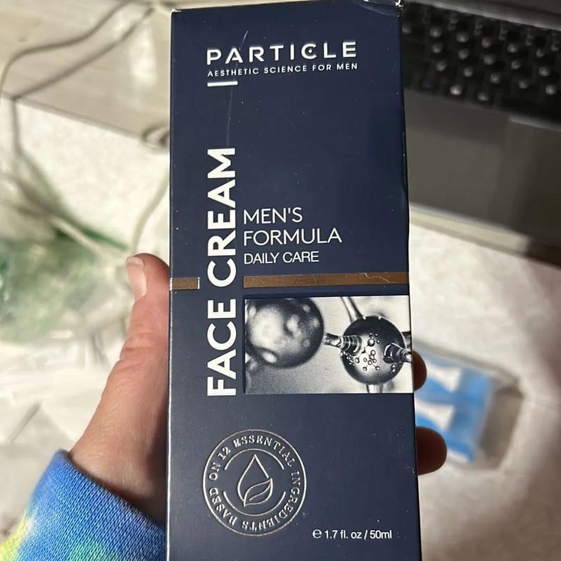 May include: A navy blue box of Particle Face Cream for men. The box features the text "FACE CREAM" vertically, and "MEN'S FORMULA DAILY CARE". It also states "Aesthetic Science for Men" and contains 50ml.
