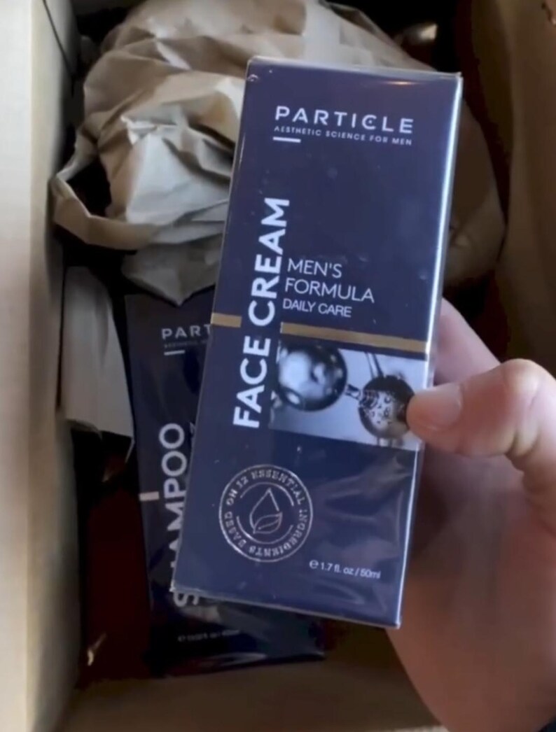 May include: A navy blue box of Particle Face Cream for men, with the text "Face Cream" and "Men's Formula Daily Care" in white. The box also includes the text "Particle Aesthetic Science for Men" and "On 12 Essential Ingredients". The product is 50ml.