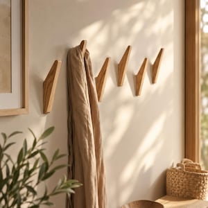 May include: A series of five light brown wooden wall hooks mounted in a row. The hooks have an angled, triangular shape. A long, beige fabric scarf is draped over the first hook on the left side, hanging down vertically against the wall surface.