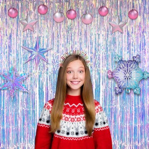 May include: A red and white patterned sweater with a reindeer motif, worn with a headband featuring the text Merry Christmas. The background consists of iridescent fringe curtains decorated with pink and silver ornaments, stars, and snowflake balloons.