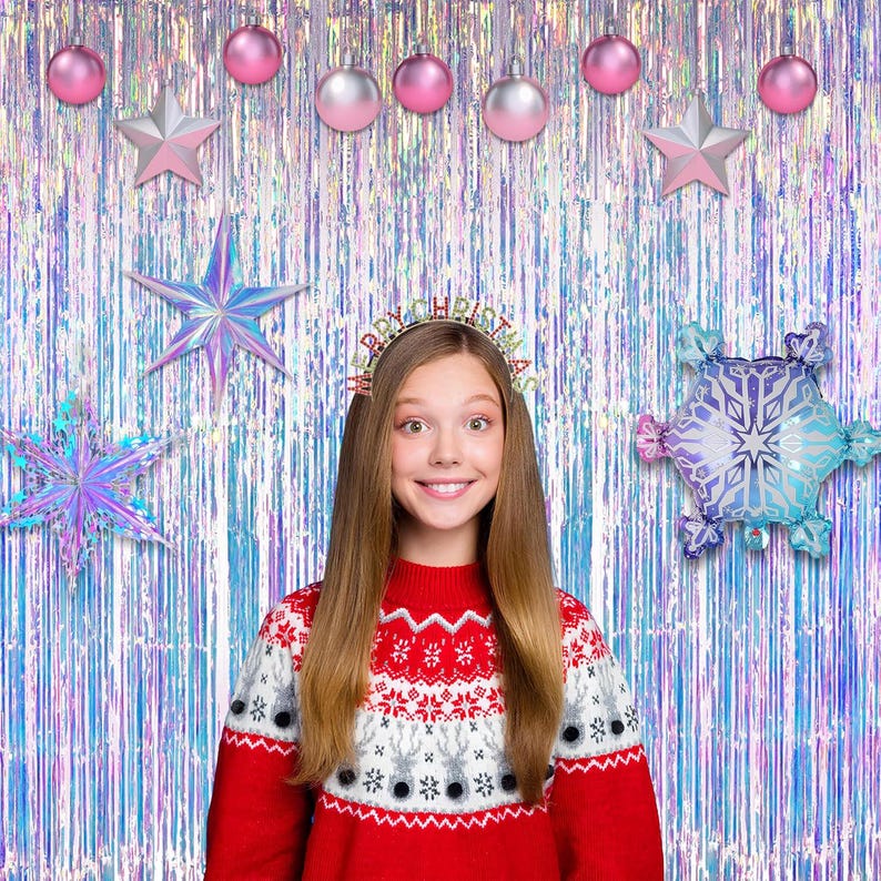 May include: A red and white patterned sweater with a reindeer motif, worn with a headband featuring the text Merry Christmas. The background consists of iridescent fringe curtains decorated with pink and silver ornaments, stars, and snowflake balloons.