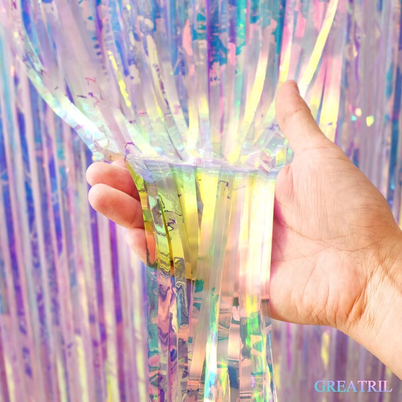 May include: A shimmering iridescent fringe curtain made of thin, vertical plastic strips that reflect light in a spectrum of colors. The material is translucent and creates a holographic effect, with the text GREATRIL printed in the bottom corner.